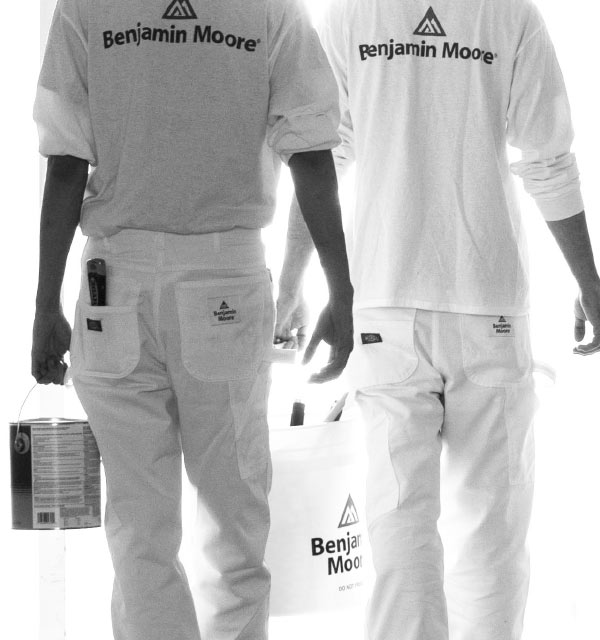 Two Benjamin Moore painters, each carrying paint and walking down a hallway with two-tone painted walls.