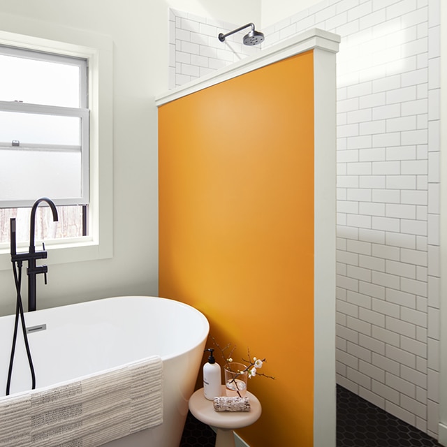 Un amusant mur d’accent orange sépare une grande douche d’une baignoire autoportante dans une salle de bains peinte en blanc avec des carreaux blancs.