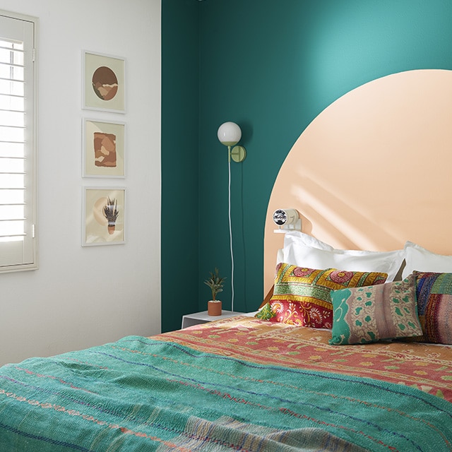 Chambre à coucher blanche avec mur d’accent vert sarcelle et demi-cercle de couleur pêche derrière un lit recouvert d’une housse et de coussins vert sarcelle et orange de style bohémien.