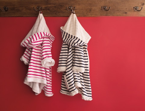 Red wall with a wooden plank coat rack, two striped children's robes, one in pink and one in black.