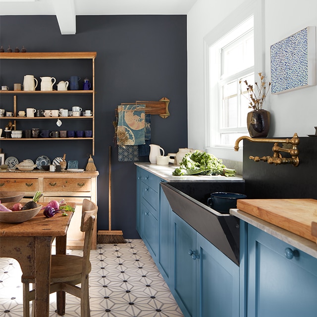 An English heritage-style kitchen with blue-painted cabinets, an accent wall painted in navy, and wood furniture.