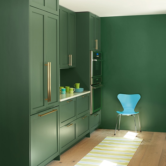 Coin cuisine épuré avec armoires et mur tout vert, plafond blanc, chaise moderne turquoise, petit tapis aux rayures jaunes sur plancher de bois blond.