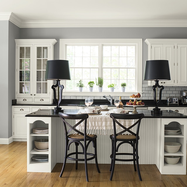 Cette cuisine gris pâle présente un éclat rafraîchissant avec ses armoires blanches et son dosseret en carreaux de céramique de la même couleur, alors que ses comptoirs noirs ajoutent un soupçon de profondeur.