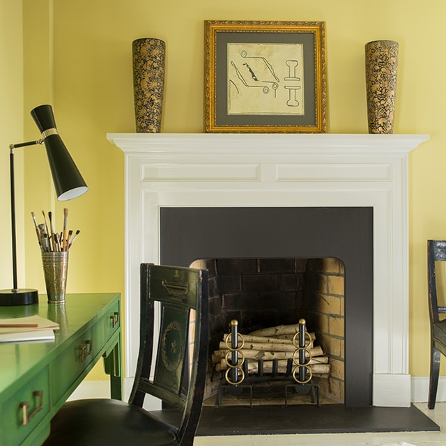 A pretty green desk and black chair contrast nicely in this yellow painted room with a white fireplace mantel, and black-and-white abstract rug.