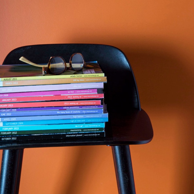 A black chair with a stack of multicoloured magazines is set off by an orange wall.