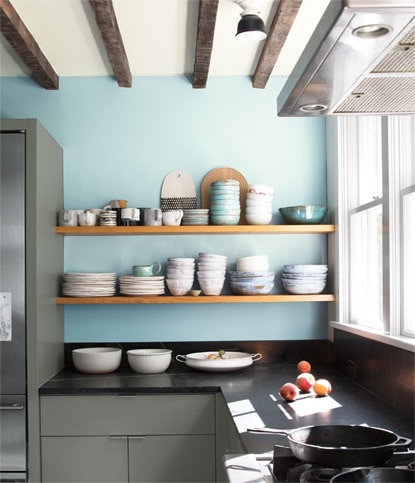 A residential kitchen with two exposed wooden shelves showcase bowls and plates against a light blue coloured wall.