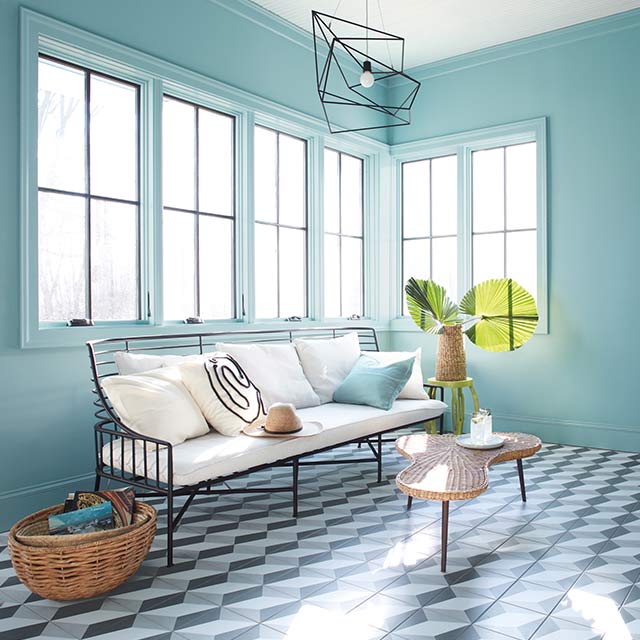 A sunroom with blue-painted walls and trim, a white ceiling, white sofa, and a black and white patterned tile floor.