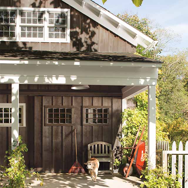 A cabin-inspired home with barn doors and wood siding stained brown, white-painted trim, and a dog on the porch.