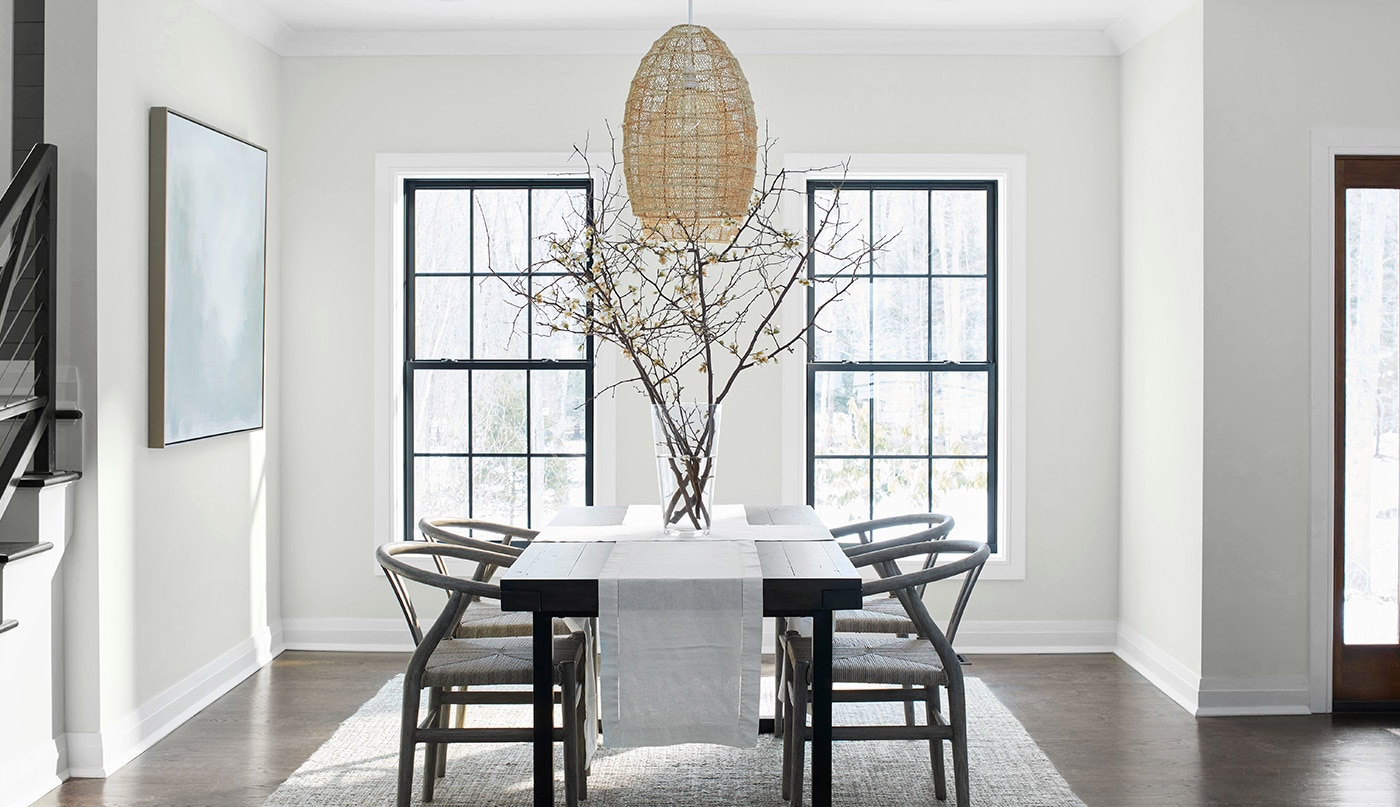 Salle à manger apaisante aux murs blanc cassé, plafond et moulures gris pâle, table noire en bois avec chaises en bois et luminaire en osier.