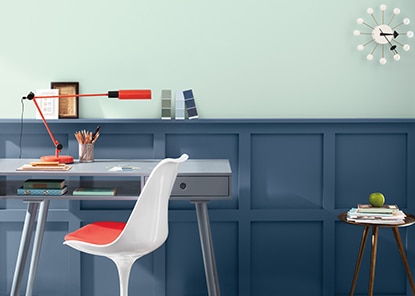Une pièce arborant des lambris peints en bleu foncé, un mur bleu clair, un bureau gris et une chaise blanc et rouge.