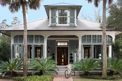 Une demeure bleu pâle de style Key West avec une véranda donnant sur un paysage tropical.
