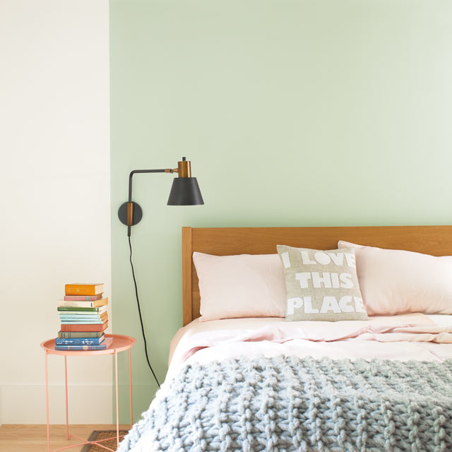 Un lit est posé contre un mur d’accent vert pâle