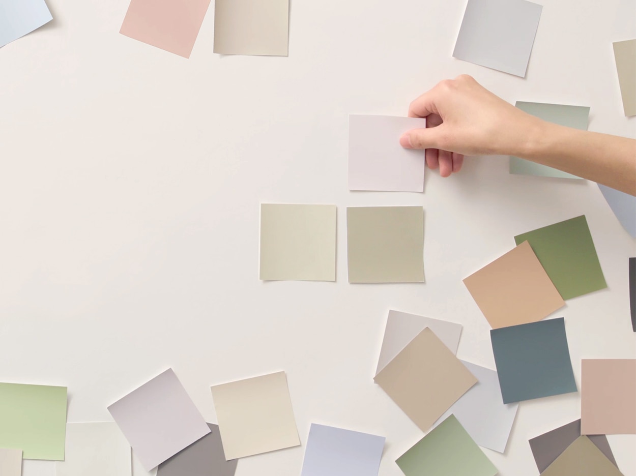 A person applying various colour swatches on a white wall.