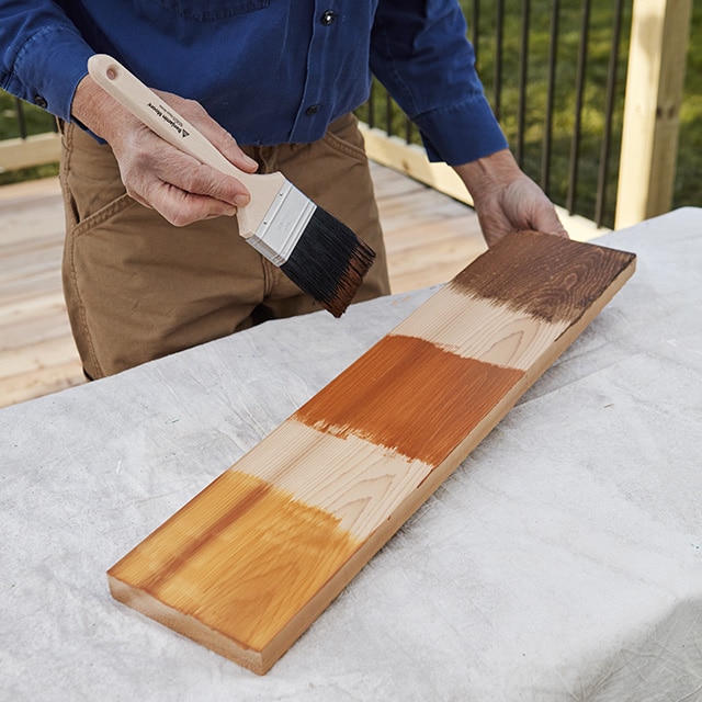 A homeowner holding a brush and piece of wood with three applied Woodluxe® Stain samples to test for colour.