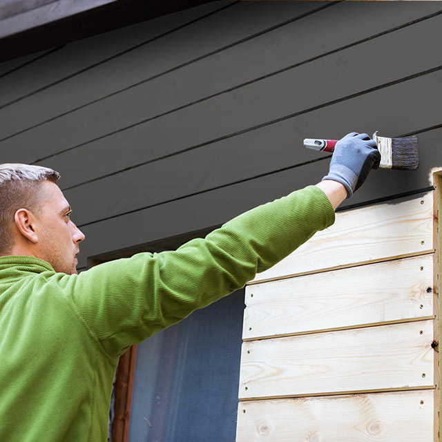 Man painting home exterior a rich black.