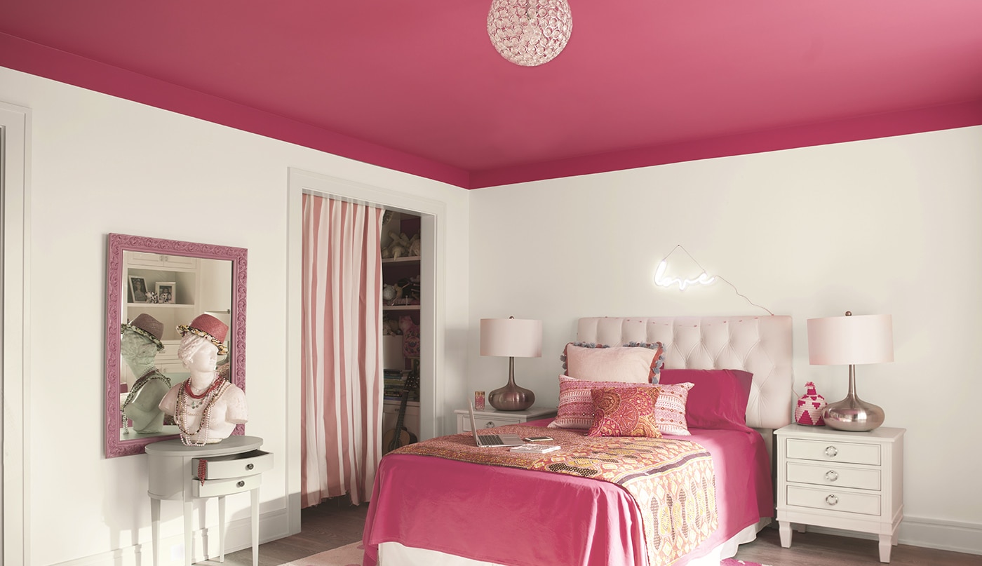 Chambre à coucher avec murs blancs, plafond rose vif et literie rose assortie avec deux tables d’appoint et des lampes.