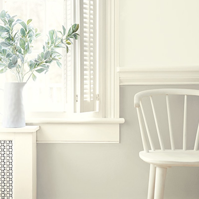 Des nuances variées de peinture blanche sur les murs, les moulures et les lambris, et une chaise blanche près de la fenêtre.