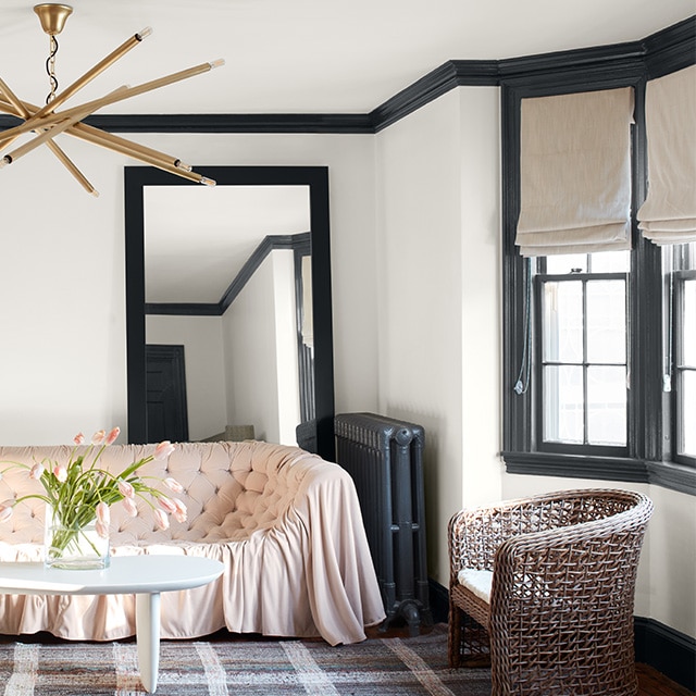 Ces moulures et ce radiateur gris foncé contrastent joliment avec les murs blancs de ce salon éclectique avec un sofa rose et un lustre moderne. 