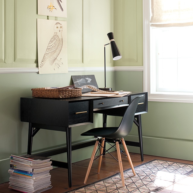 Joli espace en coin en deux tons de vert avec du lambris sur les murs du haut, des moulures blanches, et une table et une chaise noires.