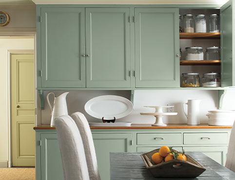 Light green cabinets add a soft glow as a backdrop to a dining table.