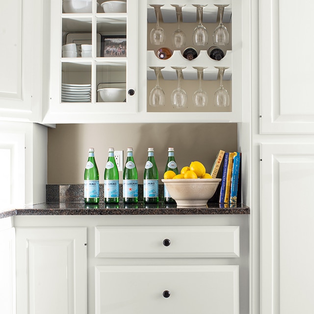 Armoires, porte-bouteilles de vin encastré et tiroirs de couleur blanche, et comptoir noir sur lequel sont posées des bouteilles d’eau et un bol de citrons. 