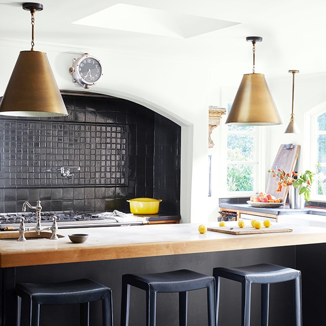 A white-painted kitchen with a black tile backsplash, black-painted island with a white countertop and pendant lights.