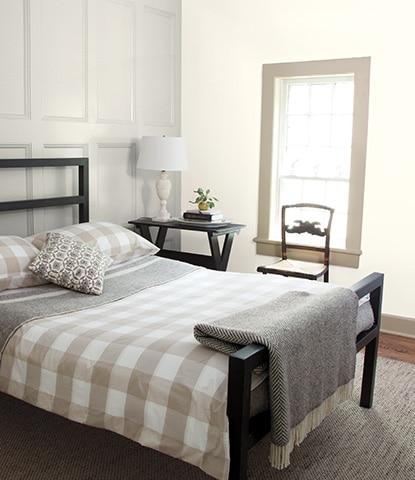 Chambre à coucher relaxante avec boiseries grises derrière un lit noir avec une literie à carreaux gris et blancs