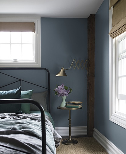 A blue bedroom painted in Black Pepper 2130-40 with exposed wood beams and a black-metal bed frame.