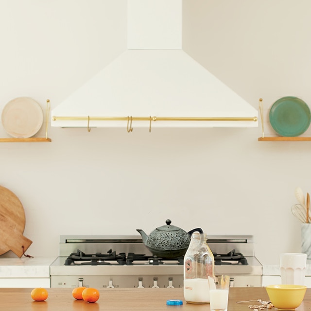 Gros plan d’une cuisine blanche montrant une hotte blanche au-dessus d’une cuisinière et des étagères ouvertes de chaque côté présentant des assiettes colorées.