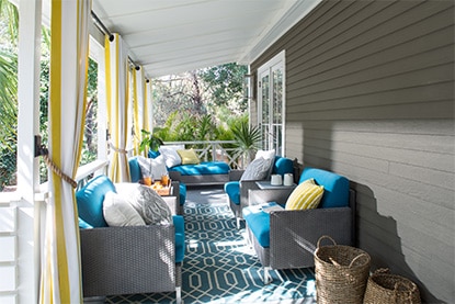 Patio couvert gris avec plafond blanc et mobilier de jardin gris assorti aux coussins bleus.