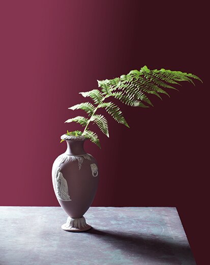 A vase sitting on a table in front of a deep red wall.