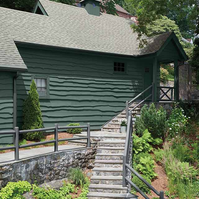 Cabin painted in deep green with gray railing and stone staircase.