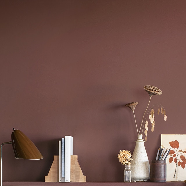 Un bureau aux murs peints en brun arborant une longue tablette en bois, un bureau et une chaise en bois assortis, et diverses décorations.