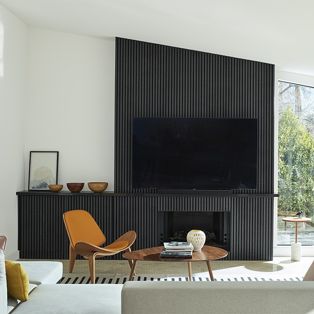 A mid-century modern style living room with bright, white-painted walls and vaulted ceiling, and a black panelled accent wall with a fireplace and large screen TV.