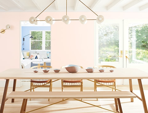Light pink-painted dining room walls with a long wooden table, matching chairs and bench seating.