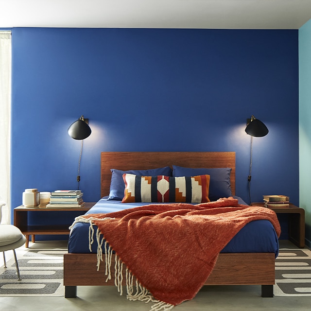 Chambre à coucher contemporaine avec mur bleu foncé, mur bleu pâle, plafond blanc, base de lit en bois et jeté de chenille rouille.
