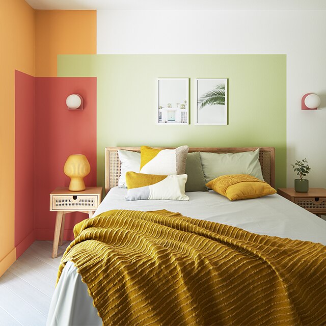 A small, contemporary bedroom with a painted colour block wall design in green, red and orange against white-painted walls, and a double bed with an orange throw.