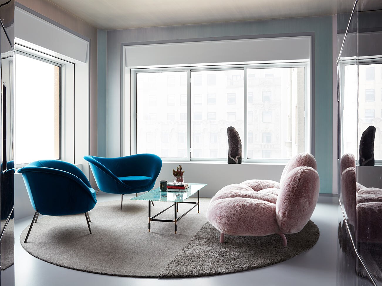 Petit salon baigné de lumière naturelle qui entre par ses nombreuses fenêtres, avec murs bleu pâle, meubles de style contemporain et petit tapis circulaire.