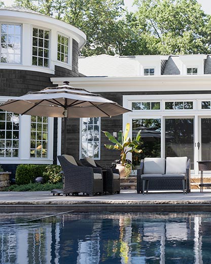 A house painted with black AURA® Exterior paint, with white trim, sliding glass doors, outdoor furniture, an umbrella, and a pool.
