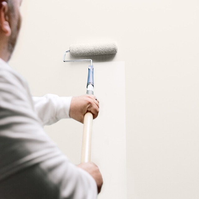 A man uses a painting roller to apply ben Interior paint on a wall.