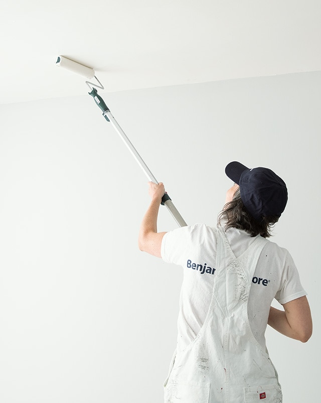 A pro painter rolls paint on a customer’s ceiling