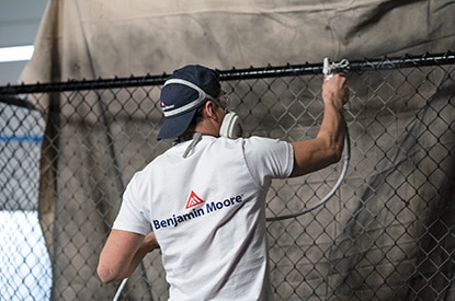 A Benjamin Moore painting contractor spray painting a metal fence using Corotech® COMMAND.