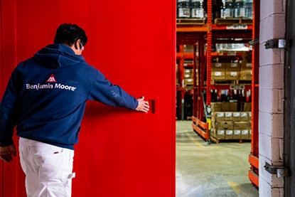 A Benjamin Moore painting contractor opening a large warehouse door painted in Corotech® COMMAND Safety Red.