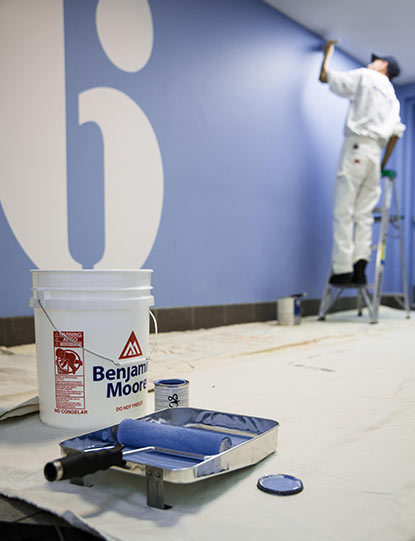 A painting contractor applies blue Benjamin Moore paint tinted with Gennex® Colour Technology to a wall.